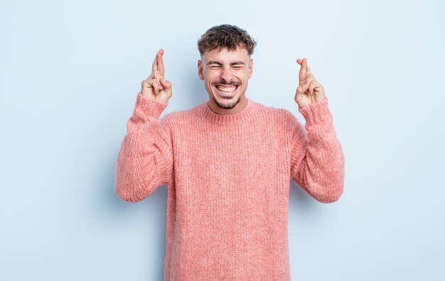 Junger gutaussehender Mann, der sich nervös und hoffnungsvoll fühlt, die Daumen drückt, betet und auf Glück hofft