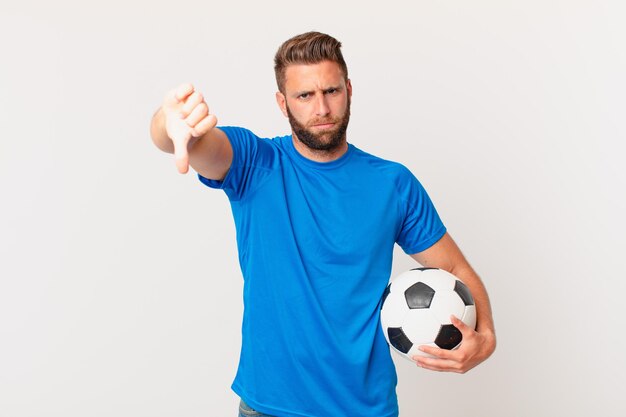 Junger gutaussehender Mann, der sich überquert und Daumen nach unten zeigt. Fußballkonzept