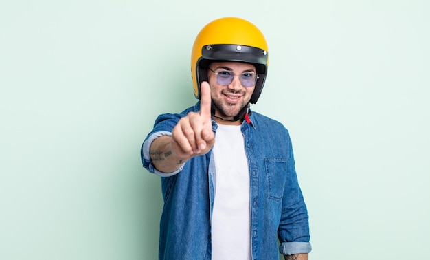 Junger gutaussehender Mann, der stolz und selbstbewusst lächelt und das Motorradhelm-Konzept Nummer eins macht