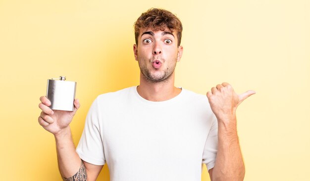 Junger gutaussehender Mann, der ungläubig überrascht schaut. Konzept der Alkoholflasche