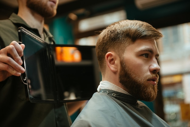 Junger gutaussehender Mann, der vom Friseur einen Haarschnitt erhält, während er im Stuhl sitzt.