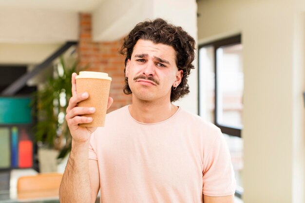 Junger gutaussehender Mann, der zu Hause ein heißes Kaffeegetränk hält