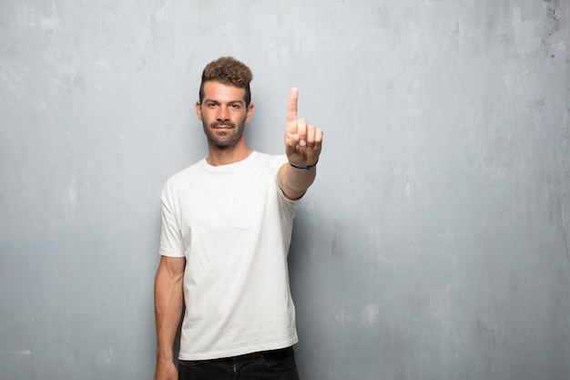 Junger gutaussehender Mann, der zufrieden gestellt und glücklich, Zahl mit einem Finger zu zählen lächelt und schaut.