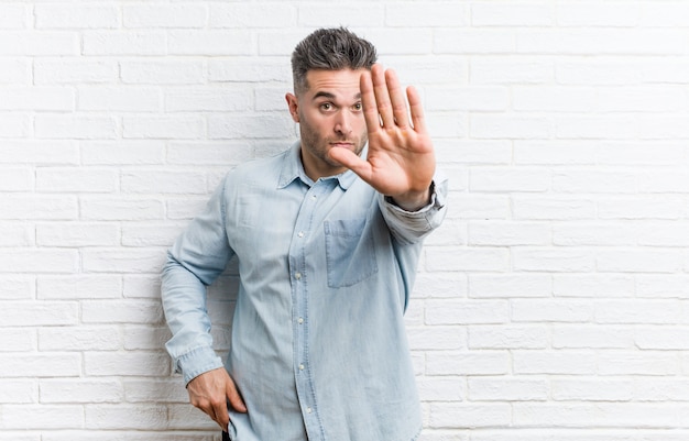 Junger gutaussehender Mann gegen eine Backsteinmauer, die mit der ausgestreckten Hand zeigt das Stoppschild, Sie verhindernd steht.