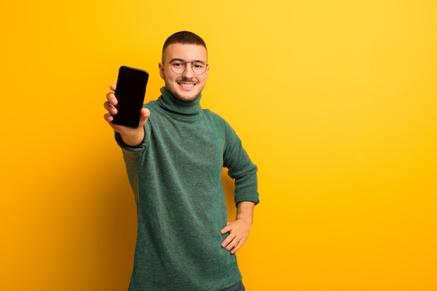 Junger gutaussehender Mann gegen flache Wand mit einem intelligenten Telefon