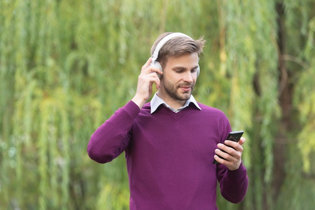 Junger gutaussehender Mann hört Musik über Kopfhörer und chattet auf dem Smartphone im Freien