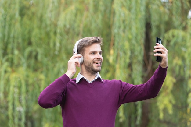 Junger gutaussehender Mann hört Musik und macht Selfie am Telefon im Freien
