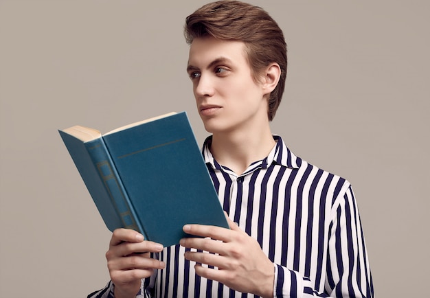 Junger gutaussehender Mann in gestreiftem Hemd ein Buch auf grauem Hintergrund lesend