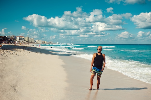 Junger gutaussehender Mann in schwarzem T-Shirt und Sonnenbrille, der den Tag am Strand genießt