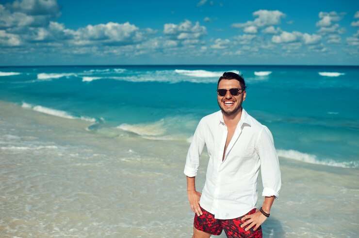 Junger gutaussehender Mann in weißem Hemd und Sonnenbrille, der den Tag am Strand genießt