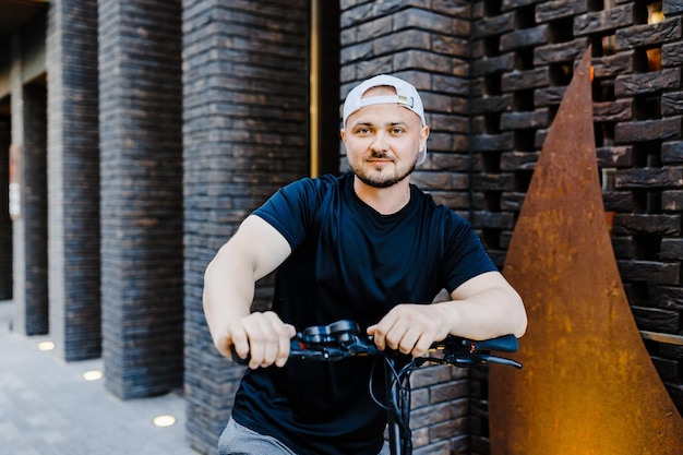 Junger gutaussehender Mann in weißer Baseballkappe, der auf Roller fährt, um entlang der Straße in der Stadt zu arbeiten