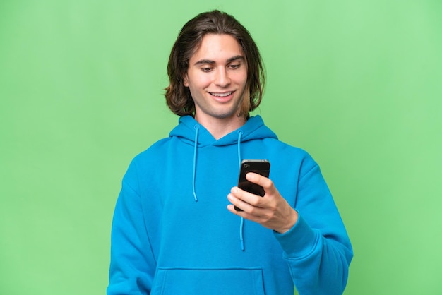 Junger gutaussehender Mann isoliert auf grünem Chroma-Hintergrund, der eine Nachricht oder E-Mail mit dem Handy sendet