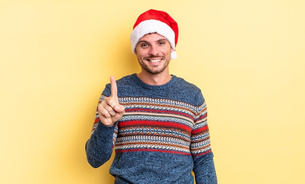 Junger gutaussehender Mann lächelt und sieht freundlich aus und zeigt die Nummer eins. Weihnachtskonzept