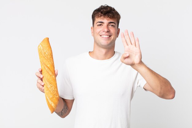 Junger gutaussehender Mann lächelt und sieht freundlich aus, zeigt Nummer vier und hält ein Brotbaguette