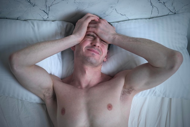 Foto junger gutaussehender mann liegt im schlafzimmer im bett und leidet unter albtraum-schlaflosigkeitskopfschmerzen