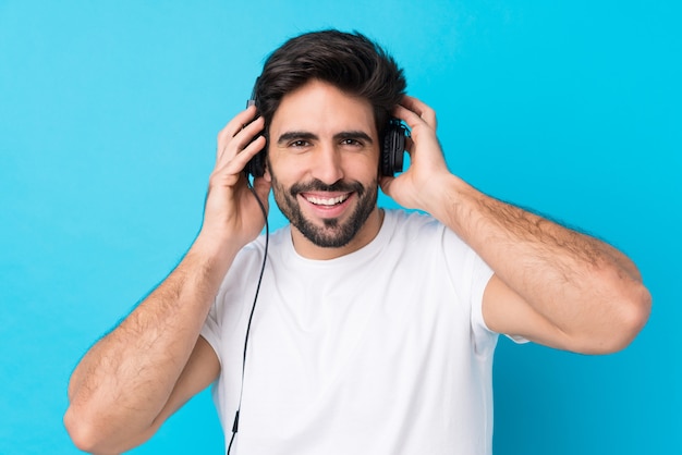 Junger gutaussehender Mann mit Bart über lokalisierter hörender Musik der blauen Wand