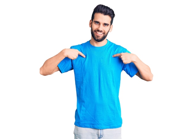 Junger, gutaussehender Mann mit Bart und lässigem T-Shirt, der selbstbewusst und lächelnd aussieht und mit stolzen und glücklichen Fingern auf sich selbst zeigt