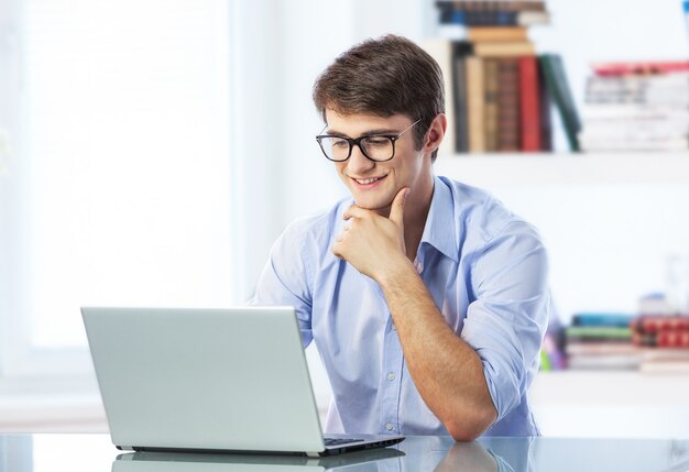 Junger gutaussehender Mann mit Brille mit Laptop