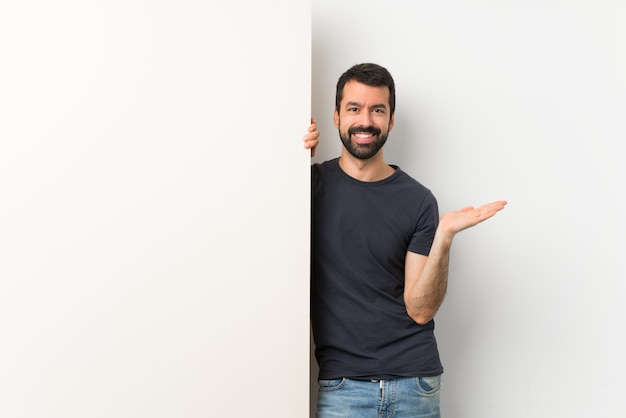 Junger gutaussehender Mann mit dem Bart, der ein großes leeres Plakat hält