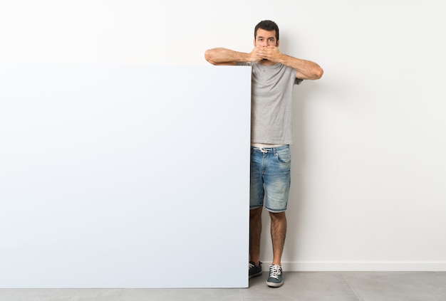 Foto junger gutaussehender mann mit dem bart, der einen großen blauen leeren plakatbedeckungsmund mit den händen hält