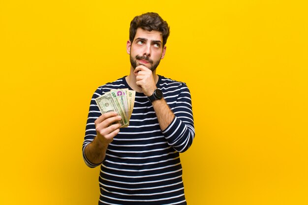 Junger gutaussehender Mann mit Dollarbanknoten gegen orange Wand