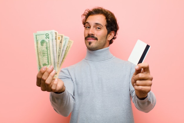 Junger gutaussehender Mann mit Dollarbanknoten gegen rosa flache Wand