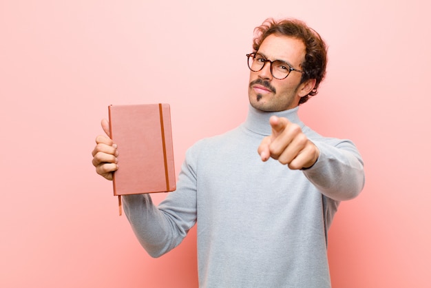 Junger gutaussehender Mann mit einem Anmerkungsbuch gegen rosa flache Wand