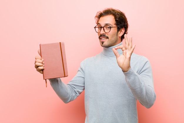 Junger gutaussehender Mann mit einem Anmerkungsbuch gegen rosa flache Wand