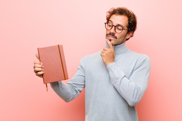 Junger gutaussehender Mann mit einem Anmerkungsbuch gegen rosa flache Wand