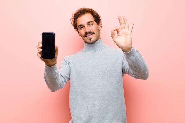 Junger gutaussehender Mann mit einem intelligenten Telefon gegen rosa flache Wand