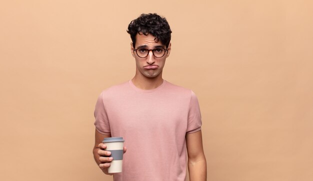 Junger gutaussehender Mann mit einem Kaffee, der traurig und weinerlich mit einem unglücklichen Blick fühlt und mit einer negativen und frustrierten Haltung weint