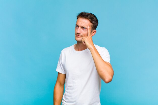 Junger gutaussehender Mann mit einem konzentrierten Blick, der sich mit einem zweifelhaften Ausdruck wundert und auf und zur Seite schaut