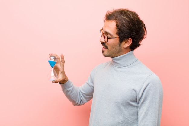 Junger gutaussehender Mann mit einem Sanduhr-Timer gegen rosa flache Wand