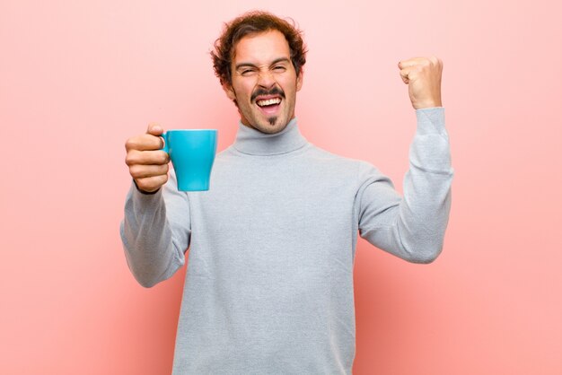 Junger gutaussehender Mann mit einer Kaffeetasse gegen rosa flache Wand