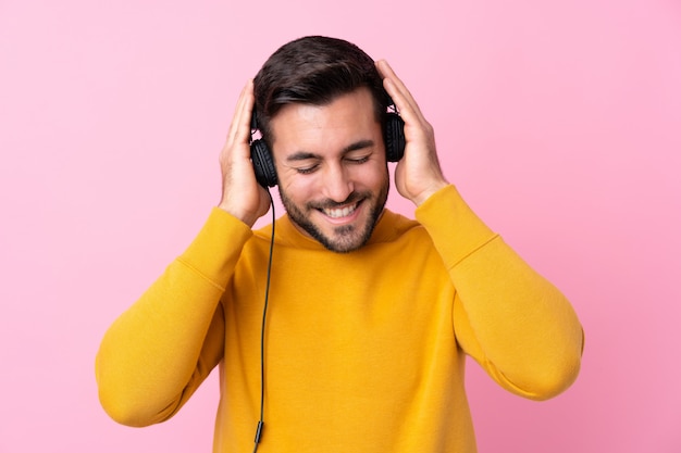 Junger gutaussehender Mann mit hörender Musik des Bartes über lokalisierter rosa Wand