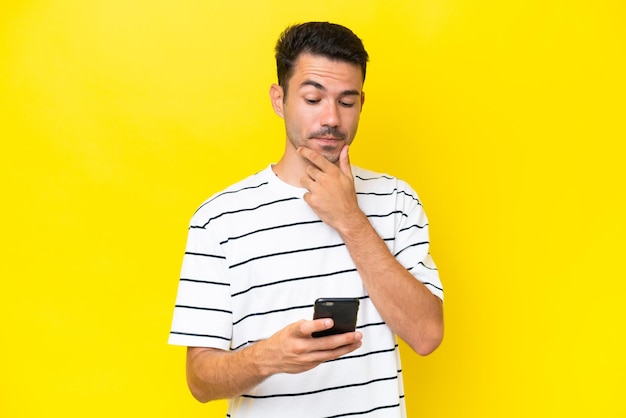 Junger gutaussehender Mann mit isoliertem gelbem Hintergrund, der denkt und eine Nachricht sendet