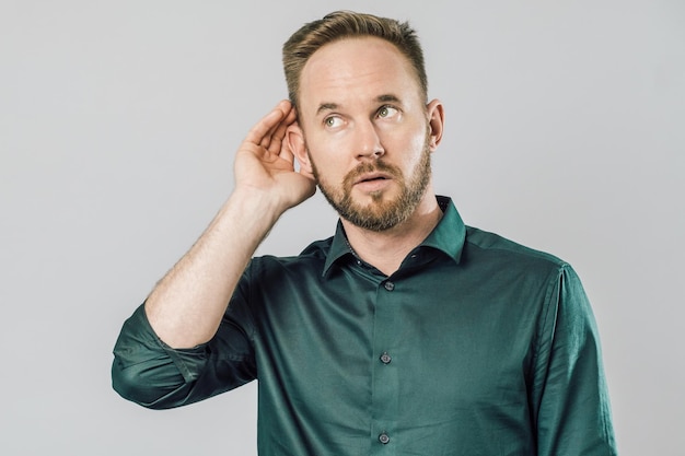 Junger gutaussehender Mann mit isoliertem grauem Hintergrund, der die Hand über dem Ohr hält und Gerüchten oder Klatsch zuhört