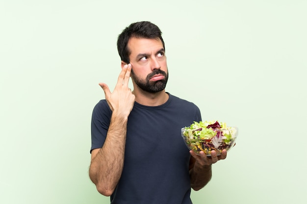 Junger gutaussehender Mann mit Salat über lokalisierter grüner Wand mit den Problemen, die Selbstmord machen, gestikulieren