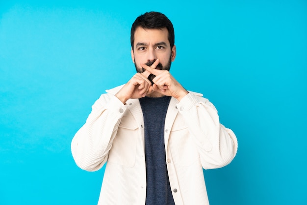 Junger gutaussehender Mann mit weißer Cordjacke über Blau, die ein Zeichen der Stille Geste zeigt