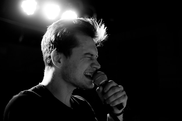 Junger gutaussehender Mann singt emotional und spricht ins Mikrofon. Schwarzweißfotografie