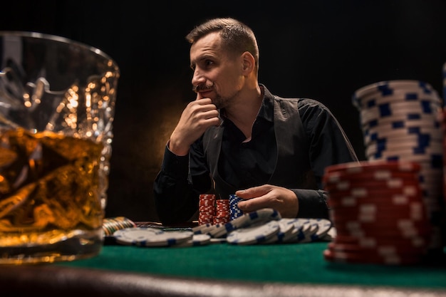 Junger gutaussehender Mann sitzt hinter Pokertisch mit Karten und Chips