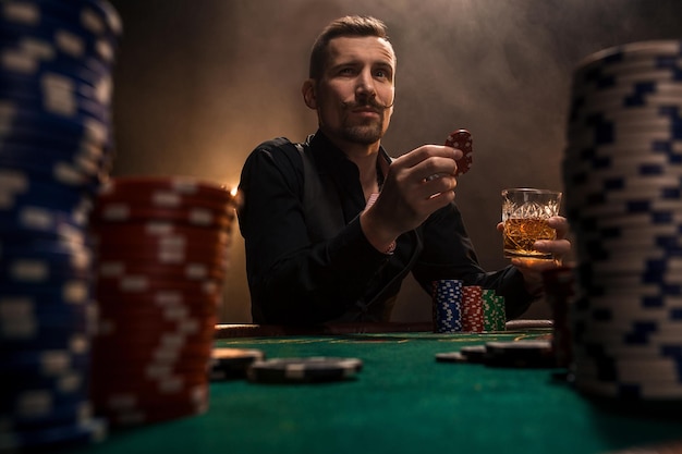Junger gutaussehender Mann sitzt hinter Pokertisch mit Karten und Chips