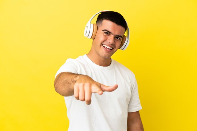 Junger gutaussehender Mann über isoliertem gelbem Hintergrund, der Musik hört