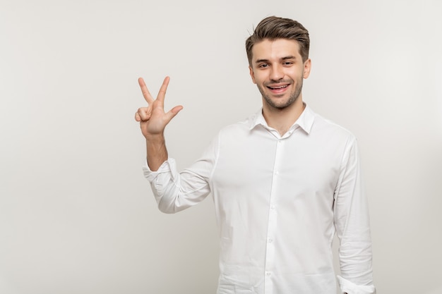 Junger gutaussehender Mann über isoliertem weißem Hintergrund mit drei Fingern beim Lächeln