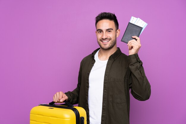 Junger gutaussehender Mann über lokalisierter purpurroter Wand in den Ferien mit Koffer und Pass