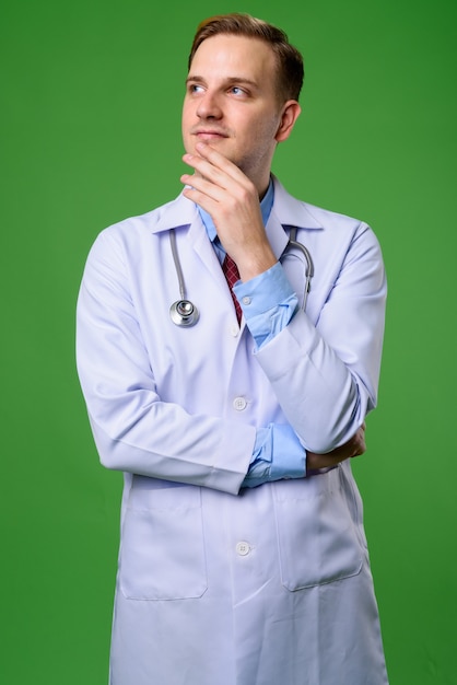 Junger gutaussehender Mannarzt mit blondem Haar gegen grünes backgrou