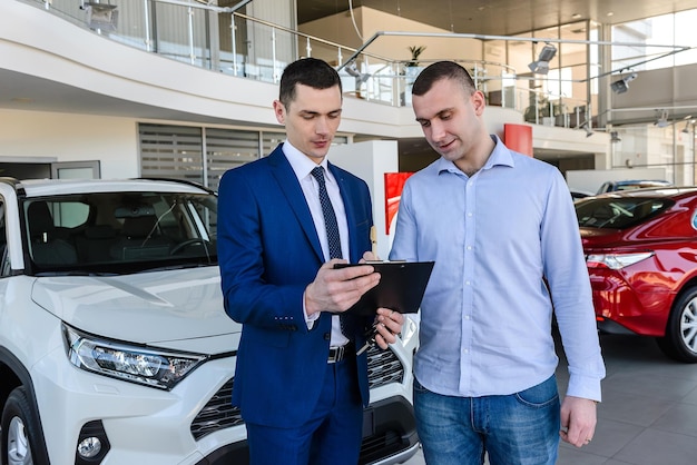 Junger Händler, der Neuwagen an männliche Kunden verkauft und Dokumente ausfüllt