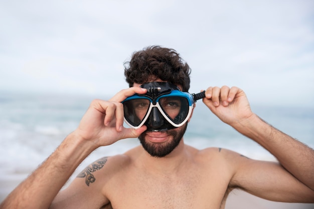 Junger hemdloser Mann am Strand mit Tauchausrüstung