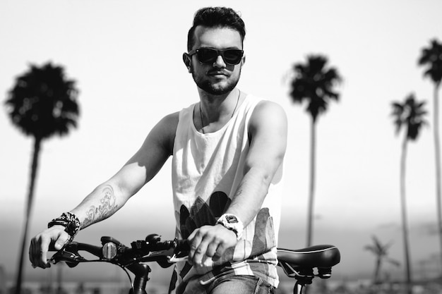 Junger Hippie-Mann auf dem Strand am sonnigen Sommertag mit Fahrrad