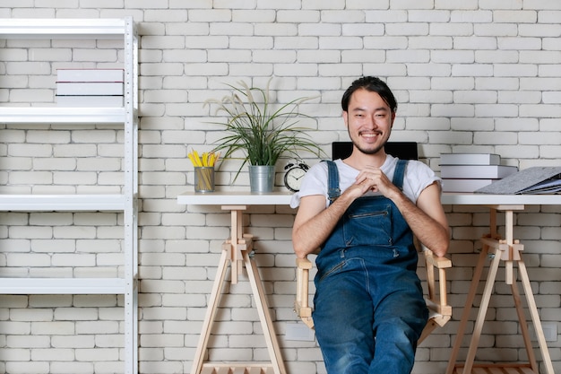 Junger Hipster-Bart-Asiat, der glücklich in seinem neuen, modernen, minimalen Startup-Büro sitzt